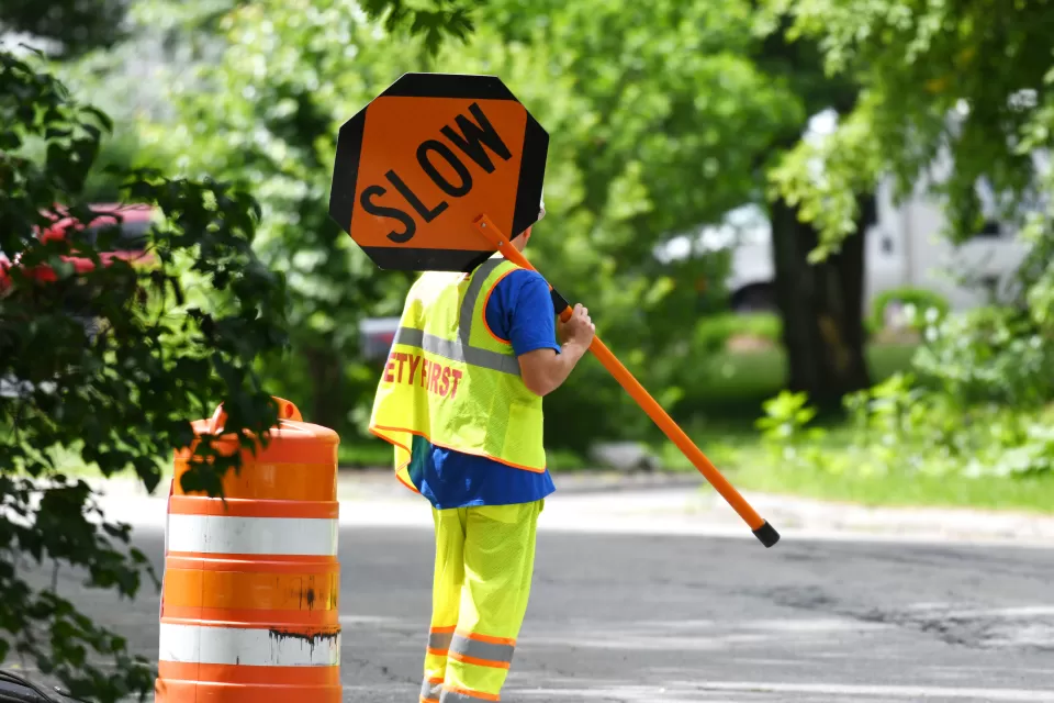 Worker in yellow safety suit holding up orange SLOW sign on road